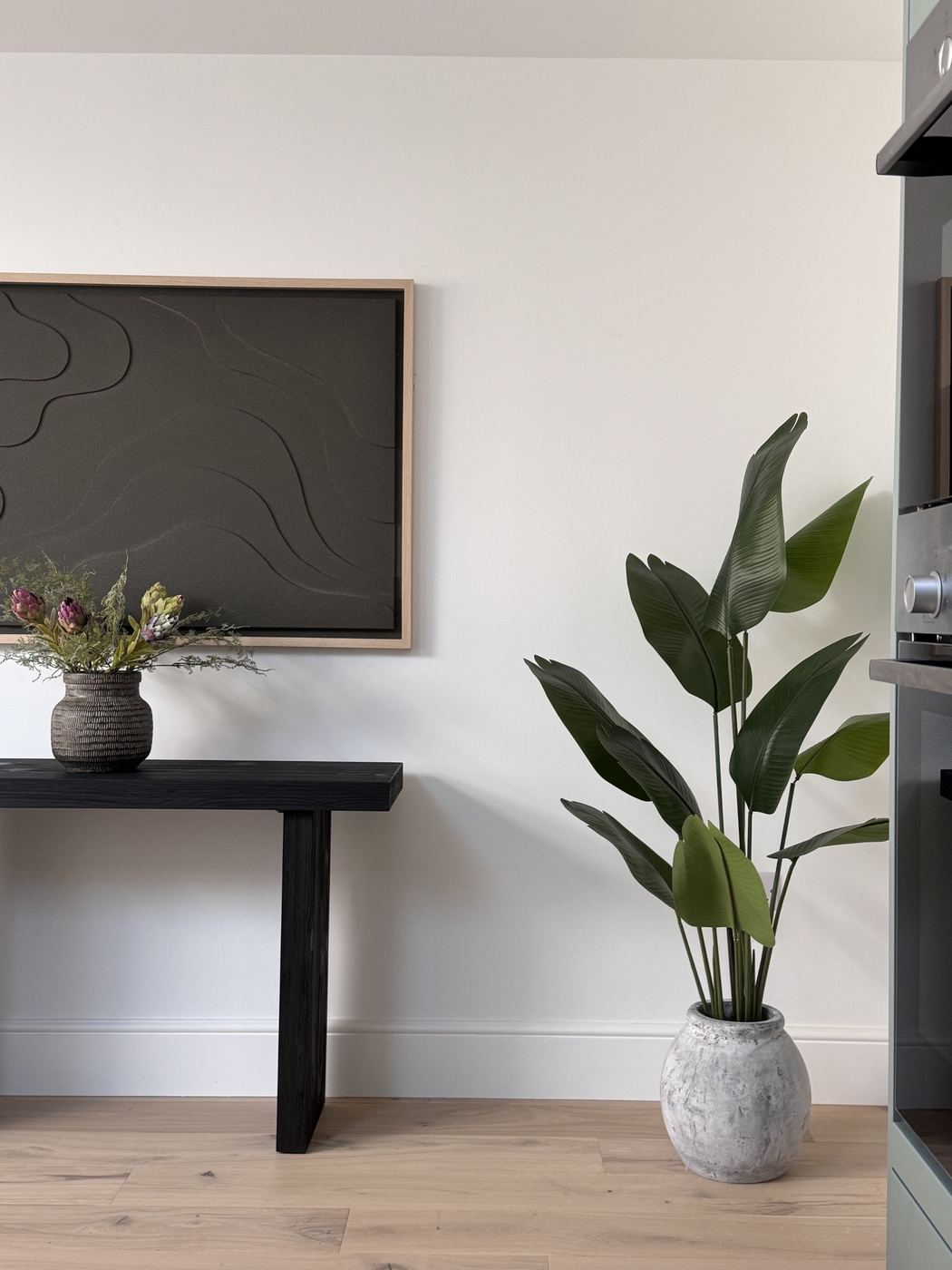 Styled interior corner with a large potted plant, console table and framed artwork
